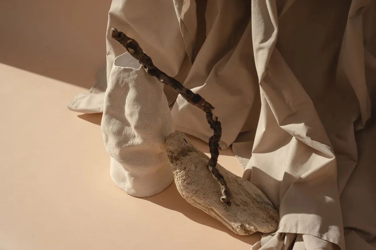 A textured ceramic vessel beside driftwood on linen