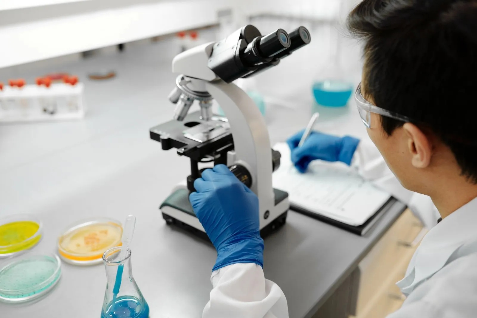 Scientist reviewing a sample under a microscope in a laboratory; illustrative photograph, not actual staff